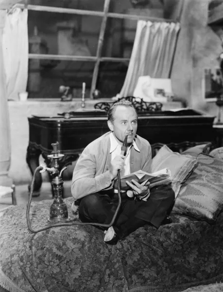 Ο άνθρωπος που κάθεται σε ένα κρεβάτι κάπνισμα του σωλήνα νερού — Φωτογραφία Αρχείου