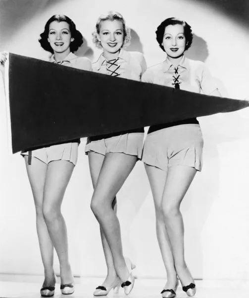 Retrato de tres mujeres jóvenes sosteniendo una pancarta y sonriendo — Foto de Stock