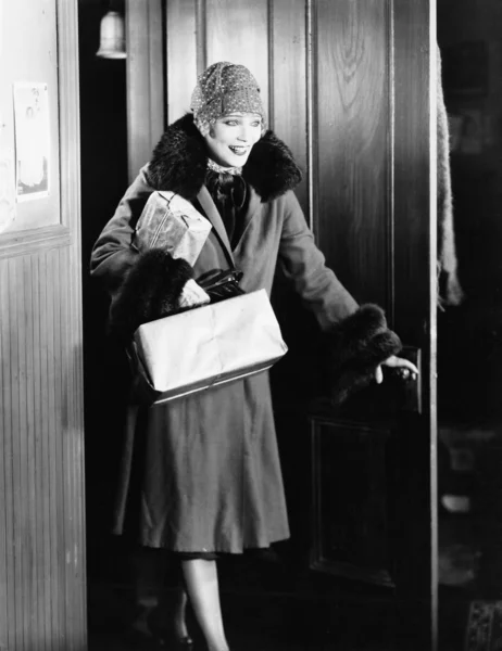 Mujer joven con abrigo y sombrero entrando en una habitación — Foto de Stock