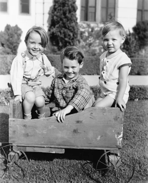 Drie jongens zitten in een kar duwen en glimlachen — Stockfoto