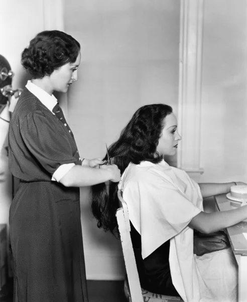 Perfil de uma cabeleireira feminina cortando o cabelo de uma jovem — Fotografia de Stock