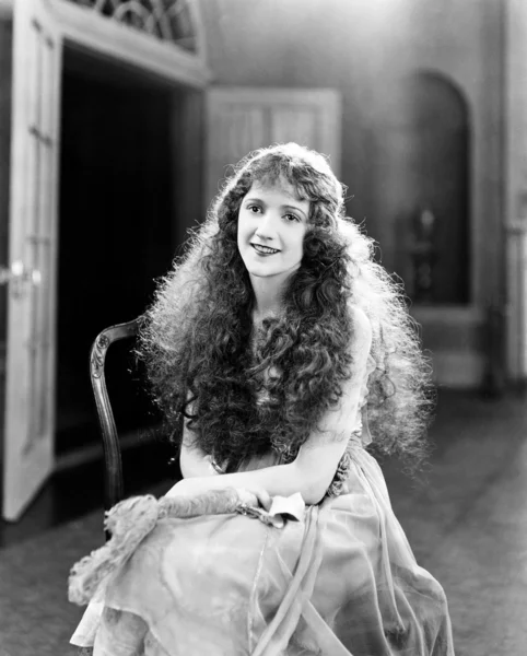 Mladá žena s dlouhé kadeře, kudrnaté vlasy, kudrnaté sedí na židli a s úsměvem — Stock fotografie