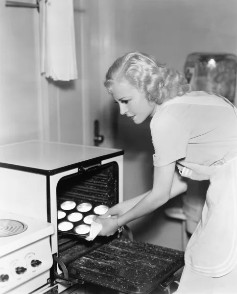 Молодая женщина берет печенье из духовки — стоковое фото