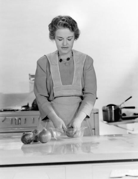 Woman peeling onions into a bowl in the kitchen