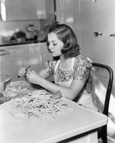 Mujer joven sentada en una silla y cortando frijoles —  Fotos de Stock