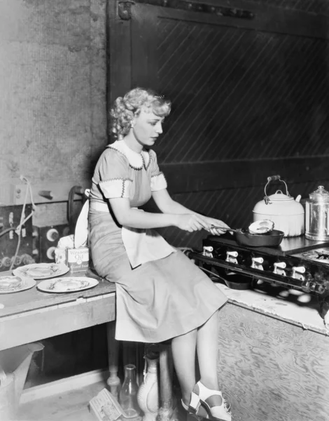 Jovem mulher sentada no balcão e cozinhar comida na cozinha — Fotografia de Stock