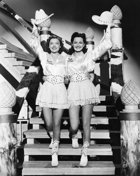 Two young women stepping down a staircase waving their western hats
