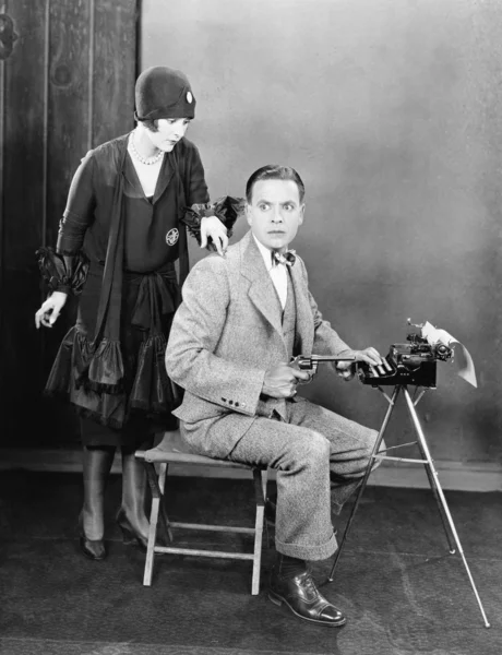 Homem em uma máquina de escrever segurando uma arma e uma mulher batendo em seu ombro — Fotografia de Stock