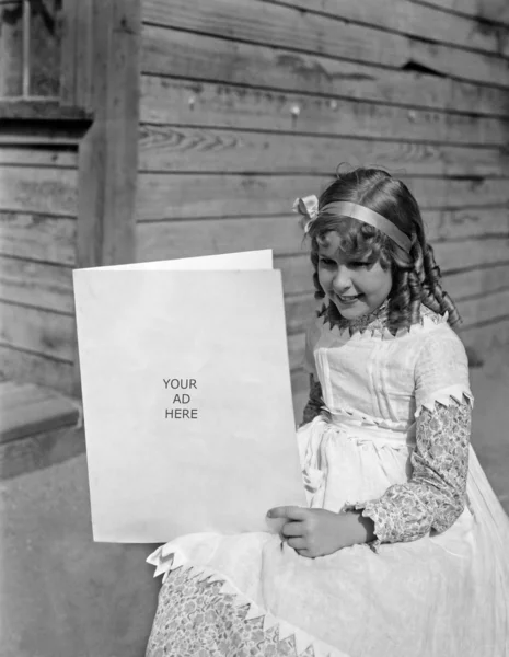 Menina em um vestido branco sentado e segurando um cartão — Fotografia de Stock