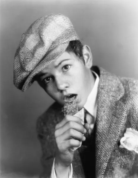 Retrato de um menino com um chapéu comendo uma barra de chocolate — Fotografia de Stock