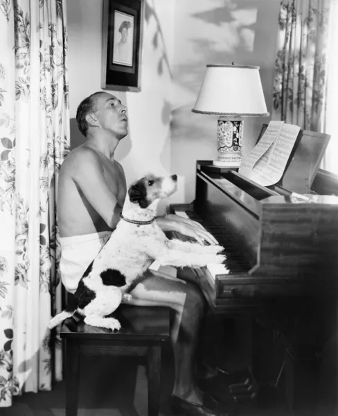 Homme jouant du piano avec son chien à côté de lui — Photo