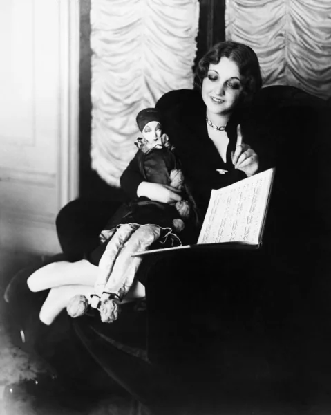 Kobieta siedzi na fotelu z jej lalek, czytanie książki — Zdjęcie stockowe