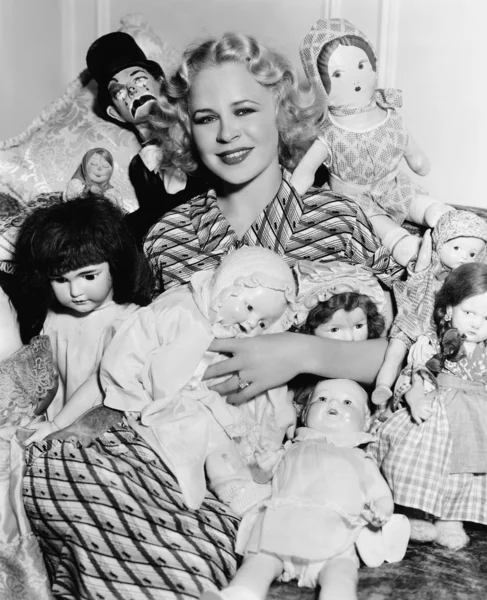 Portrait of a woman surrounded by dolls and smiling — Stock Photo, Image