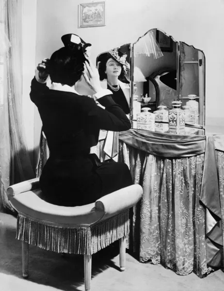 Kvinna att sätta på en hatt framför ett toalettbord — Stockfoto