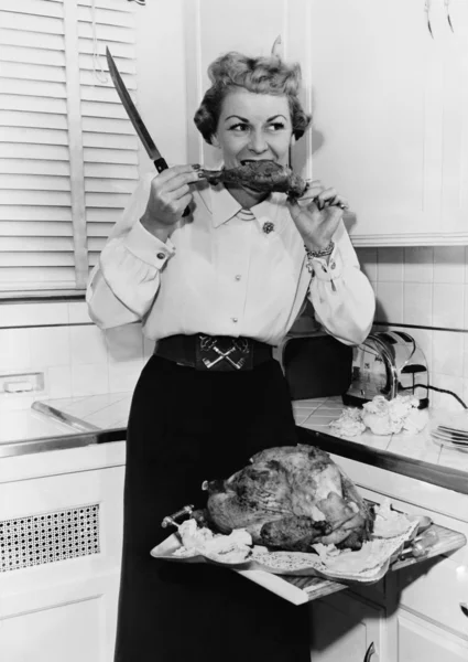Femme mangeant de la dinde rôtie dans sa cuisine avec un couteau à la main — Photo