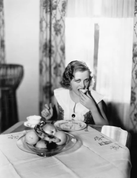 Retrato de una mujer sentada en una mesa y comiendo un pedazo de pan — Foto de Stock