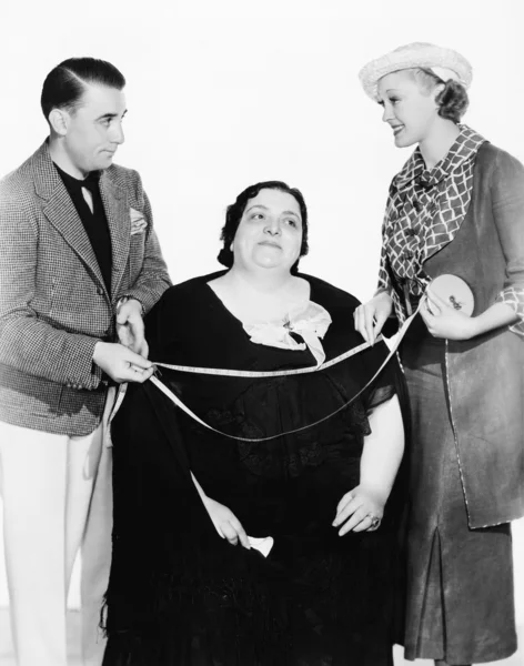Мужской портной и его ассистент измеряют толстую женщину с помощью измерительной ленты — стоковое фото