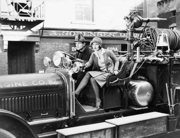 Bombeiro dirigindo um carro de bombeiros e uma jovem sentada ao lado dele — Fotografia de Stock