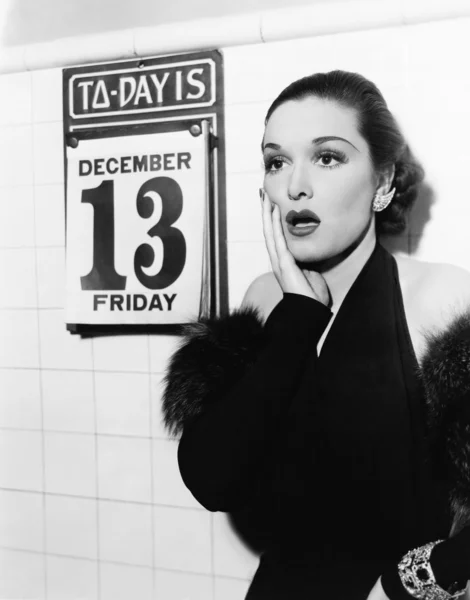 Mujer joven mirando sorprendido después de ver el viernes 13 en un calendario —  Fotos de Stock