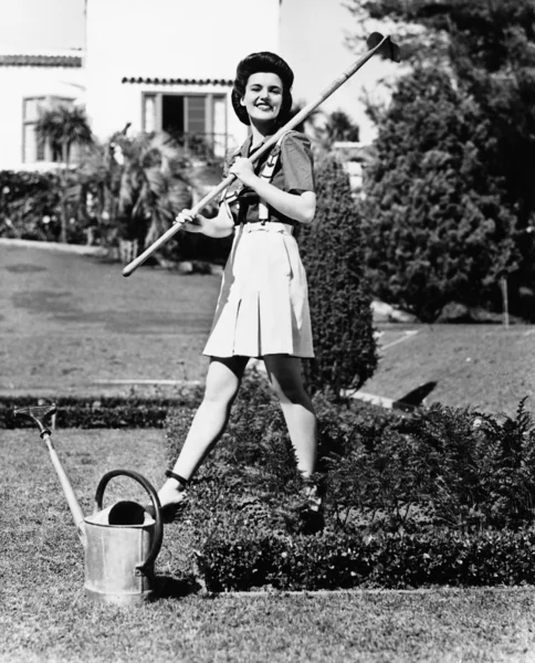 Profiel van een jonge vrouw met een hark op haar schouder in een tuin — Stockfoto