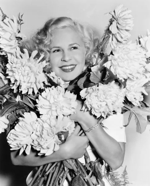 Retrato de uma jovem segurando um monte de flores que parecem felizes — Fotografia de Stock