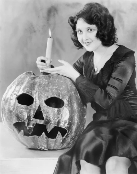 Young woman holding a burning candle on a Jack O' Lantern and smiling — Stock Photo, Image