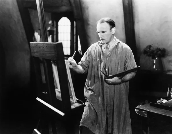 Man painting on an easel with a paintbrush — Stock Photo, Image