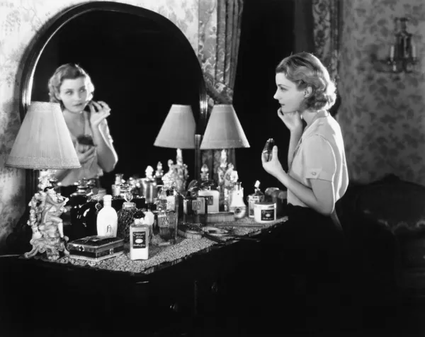 Mujer joven delante de su vanidad aplicando maquillaje —  Fotos de Stock