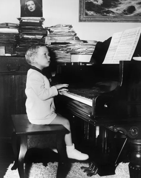 Perfil de un chico sentado en un taburete y tocando un piano — Foto de Stock