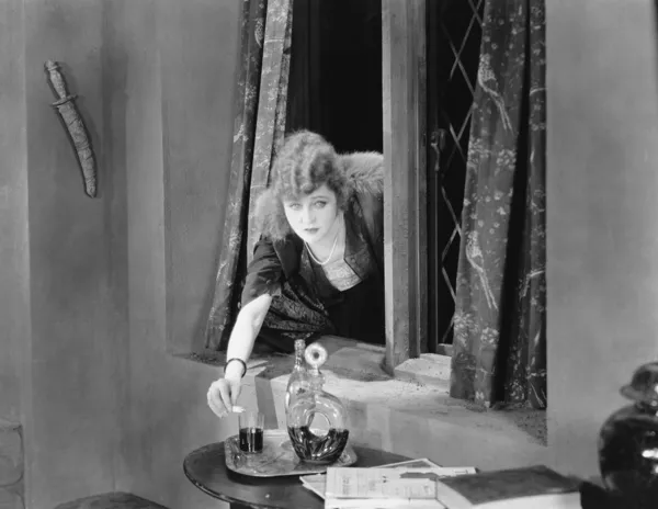 Πορτρέτο του μια νεαρή γυναίκα που φθάνει μέσα από ένα παράθυρο και να ρίχνει δηλητήριο σε ένα ποτήρι — Φωτογραφία Αρχείου