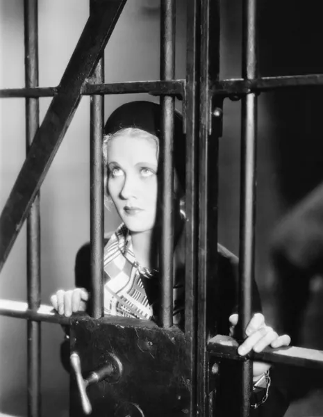 Ung kvinna som står bakom galler i en fängelsecell — Stockfoto