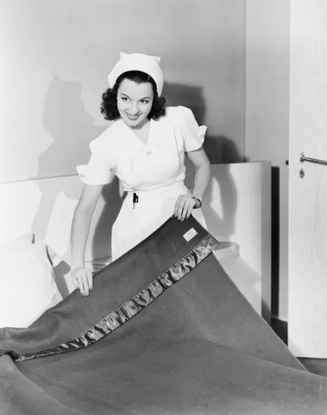 Женщина-медсестра заправляет кровать в больнице и улыбается — стоковое фото