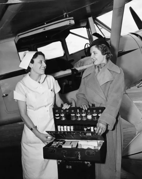Female nurse with a young woman standing in front of an airplane and opening a medicine box — Stock Photo, Image