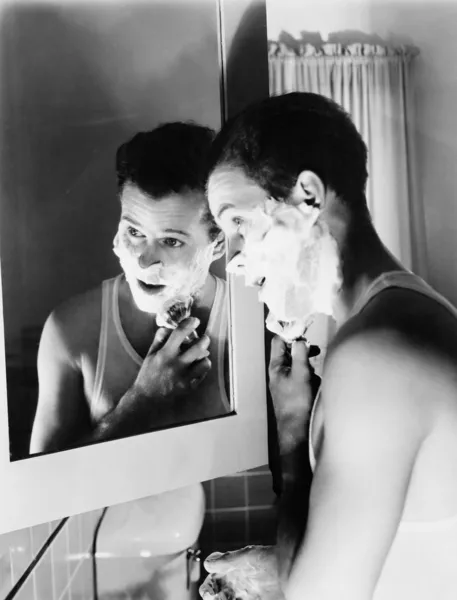 stock image Profile of a young man in front of a mirror in a bathroom shaving