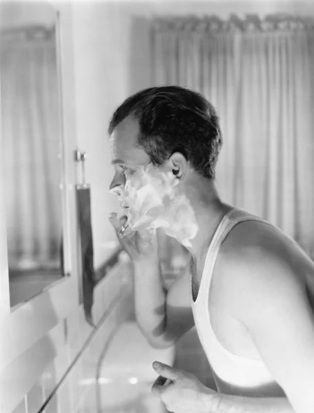 Perfil de um jovem na frente de um espelho em um banheiro de barbear — Fotografia de Stock
