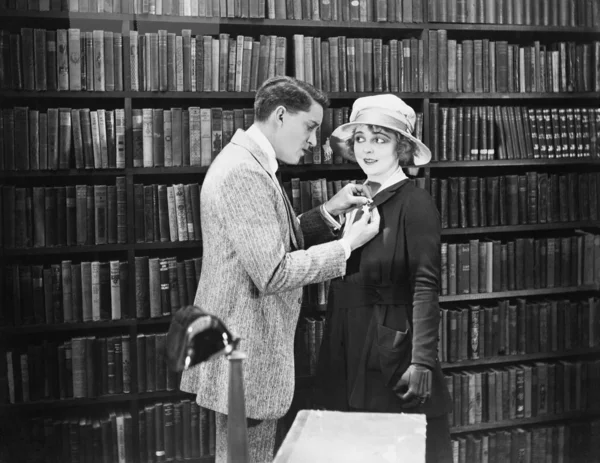Profil eines jungen Mannes, der in einer Bibliothek eine Brosche am Mantel einer jungen Frau befestigt — Stockfoto