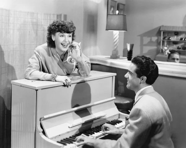 Профиль молодого человека, играющего на пианино с молодой женщиной, стоящей перед ним и улыбающейся и поющей — стоковое фото
