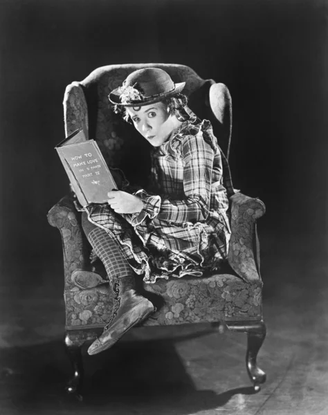 Profil eines Mädchens, das in einem Sessel sitzt und ein Buch hält — Stockfoto