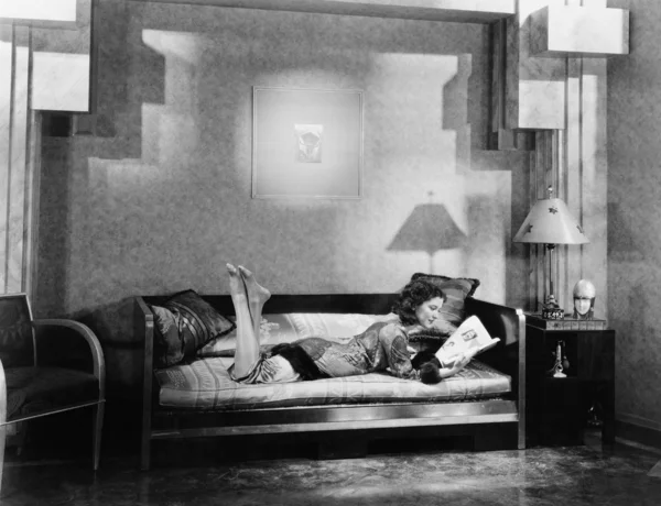 若い女性がソファに横たわって雑誌を読んで — ストック写真