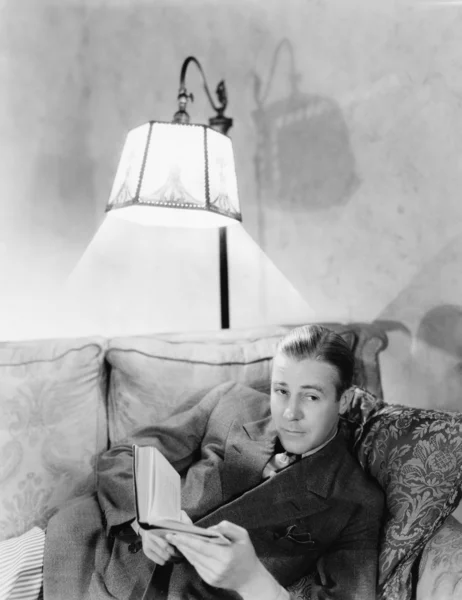 男子躺在沙发上，拿一本书 — 图库照片