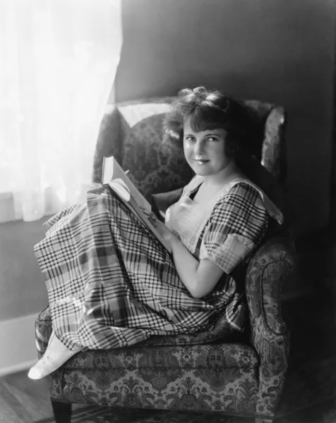 Portrét mladé ženy sedí v křesle a drží knihu — Stock fotografie