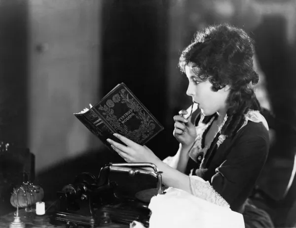 一名年轻女子坐在和读一本书和吃的配置文件 — 图库照片