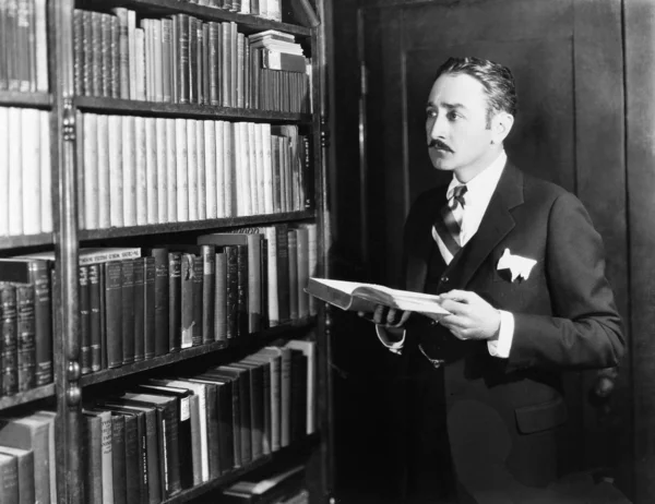 Hombre seleccionando libros de estantería en una biblioteca — Foto de Stock