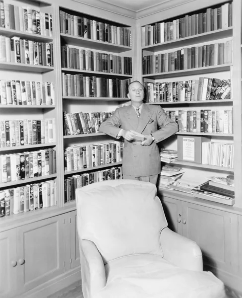 Man leaning against a bookshelf in a library — Stock Photo, Image