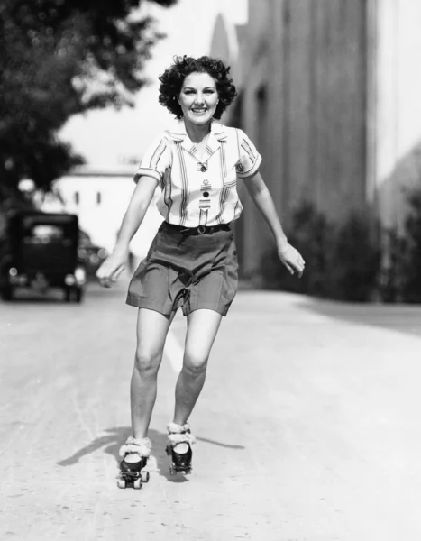 Portret van een jonge vrouw schaatsen op de weg en glimlachen — Stockfoto