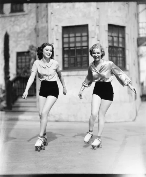 Две молодые женщины катаются на роликах по дороге и улыбаются — стоковое фото