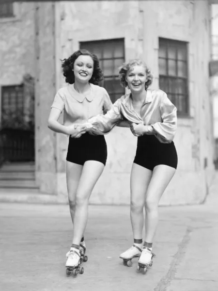 Портрет двух молодых женщин с роликовыми коньками на дороге и улыбающихся — стоковое фото