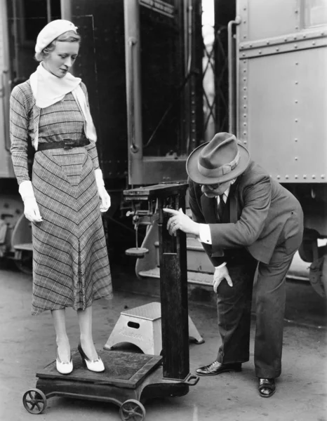 Профиль мужчины, измеряющего вес женщины, стоящей на весах перед поездом — стоковое фото
