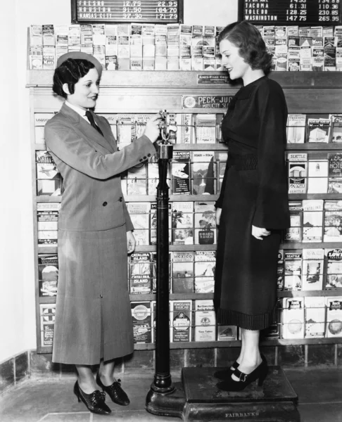 stock image Profile of a young woman in an uniform measuring weight of another young woman on a weighing scale