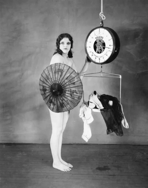 Retrato de una joven parada frente a una báscula de pesaje y escondida con una sombrilla — Foto de Stock